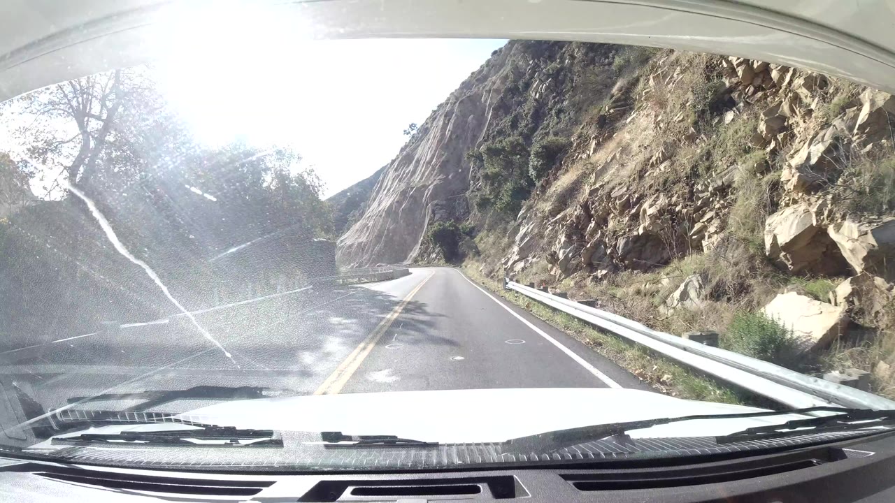 Windshield view of road passing a steep rocky canyon wall.