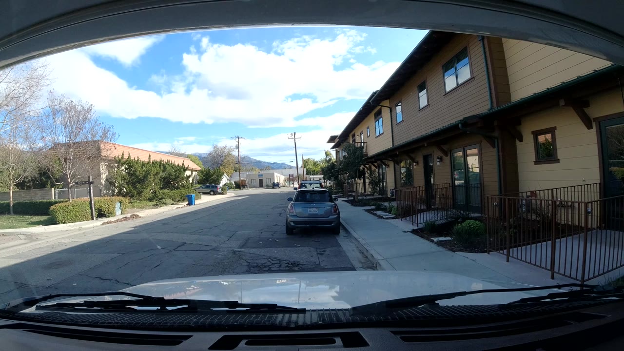 Quiet street with parked car, sidewalk, trees, and building railings