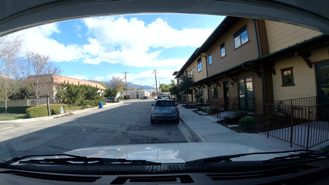 One second into the Ojai, California clip, the windshield frames the same residential block with the parked car slightly centered, sidewalk and railings at right, and no visible people.