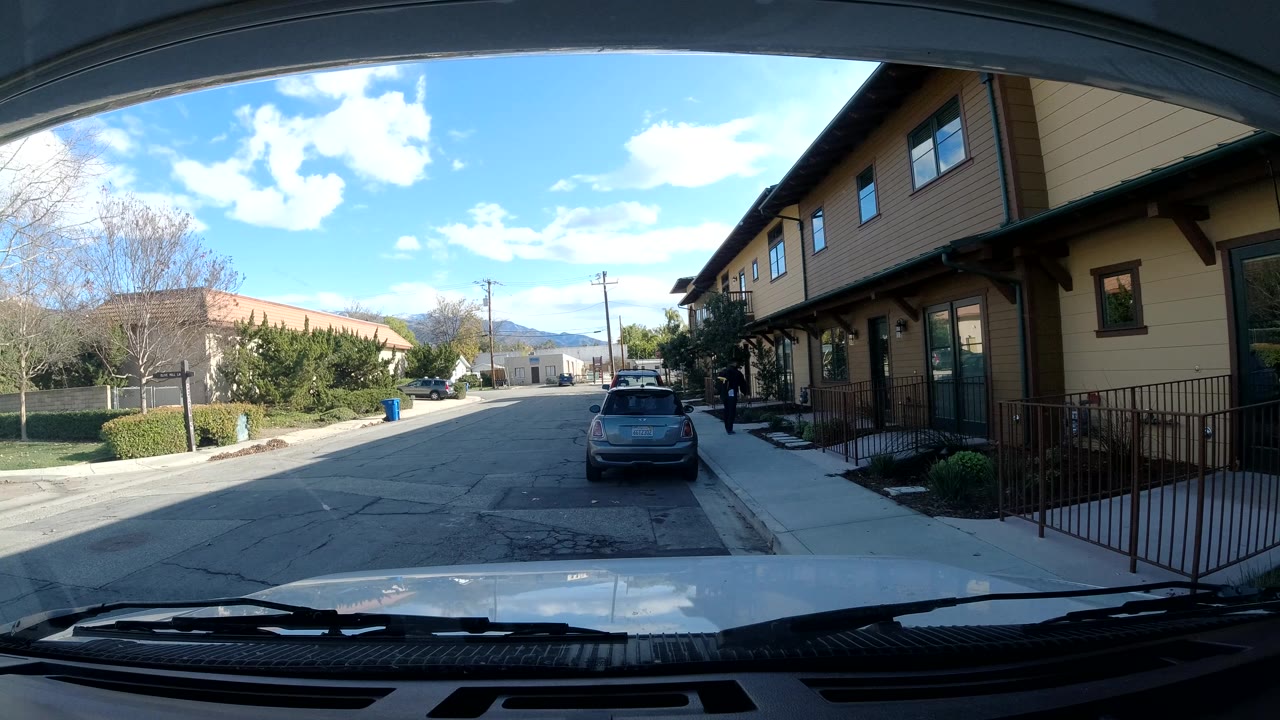 Third frame shows the Ojai street from the same windshield angle, with a small dark figure near the right-side building, the parked hatchback ahead, trees at left, and bright sky above.