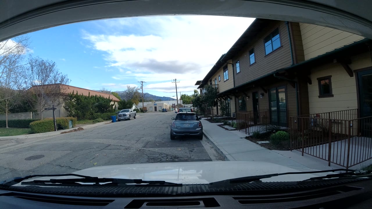 Windshield view of a quiet road beside residential buildings.