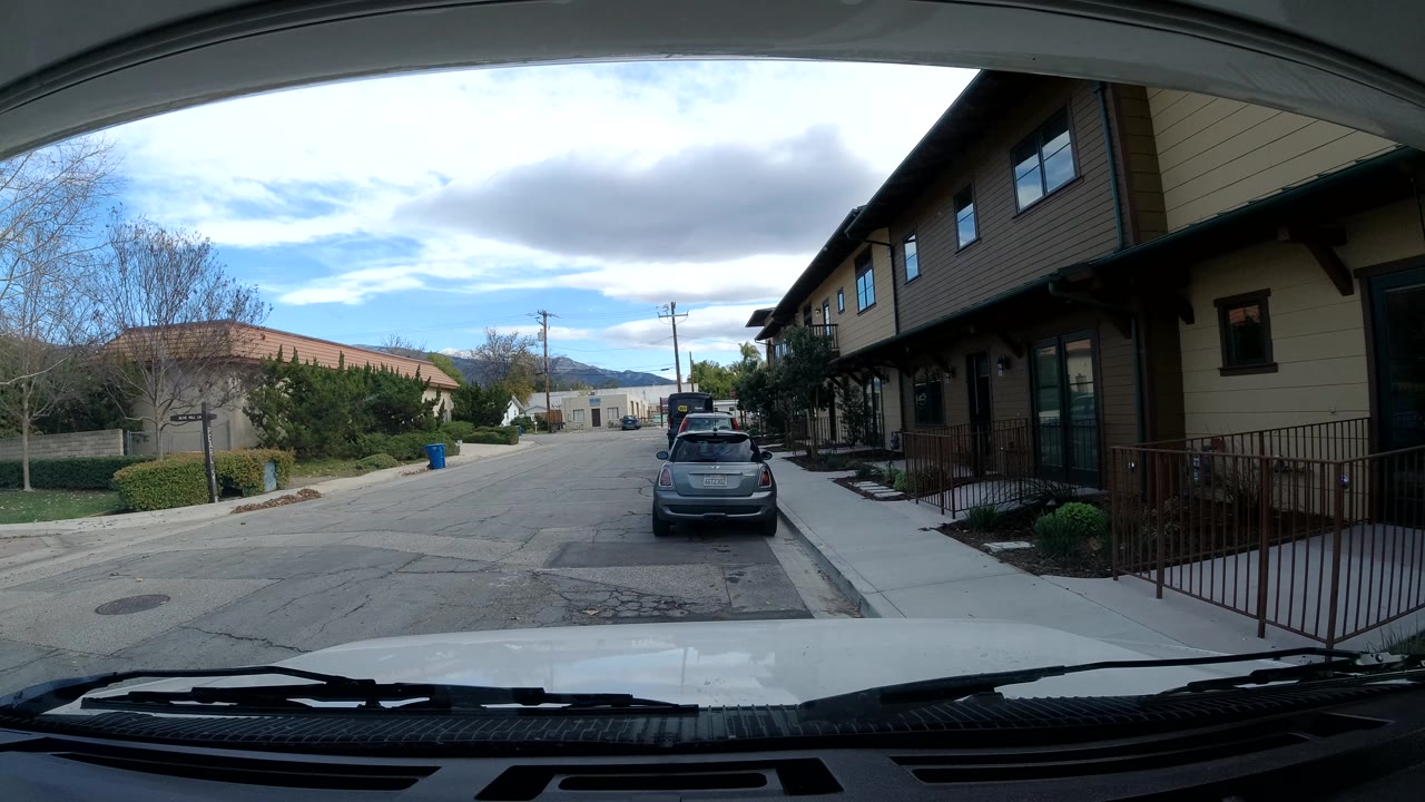 Car-mounted street view with a parked car and residential buildings along the right side.