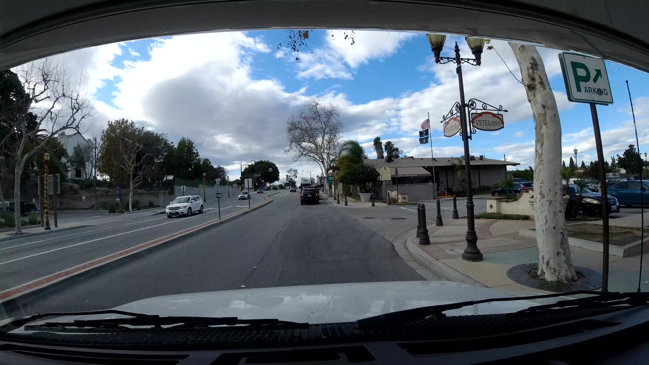 Street view with storefront signs, parked cars, and a parking sign.