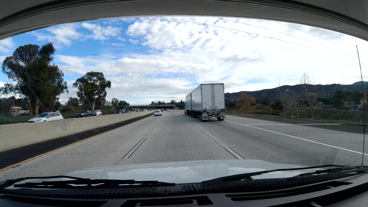 Highway traffic with a white truck ahead and cars near a tree-lined median.