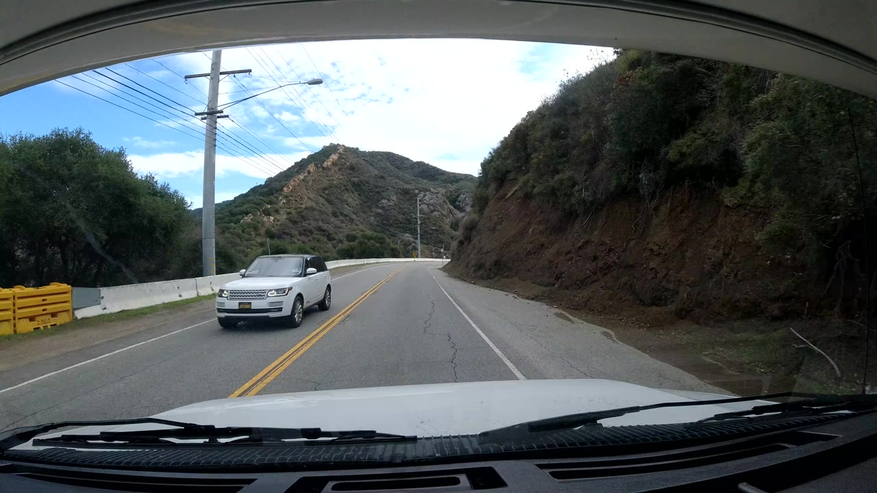Oncoming white SUV on a two-lane road near a utility pole and hillside.