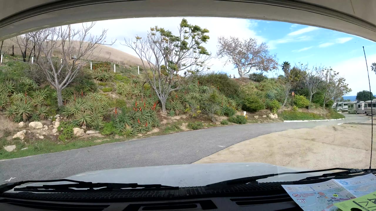 Road bends beside planted hillside with distant vehicles at right