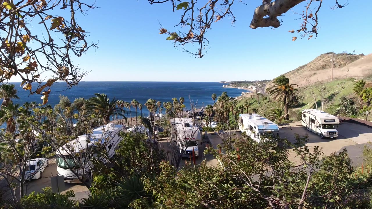 Coastal overlook with ocean horizon, palm trees, RVs, and hillside