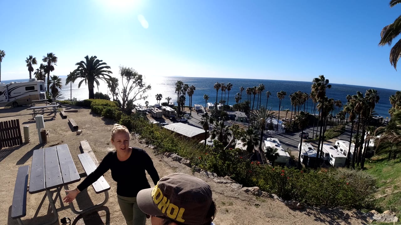 Woman beside a picnic table with another person partly visible.