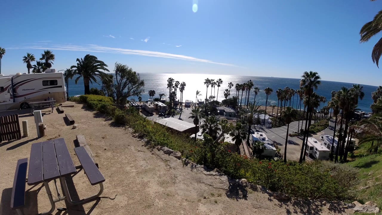 Third frame from Malibu, California holds the RV and picnic area at left, with palms and parked vehicles below the slope and no visible people.