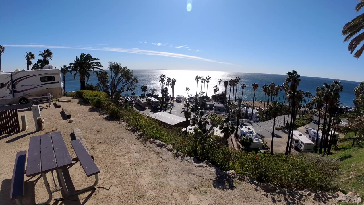 Picnic table above parked RVs and palm trees facing a bright ocean view.