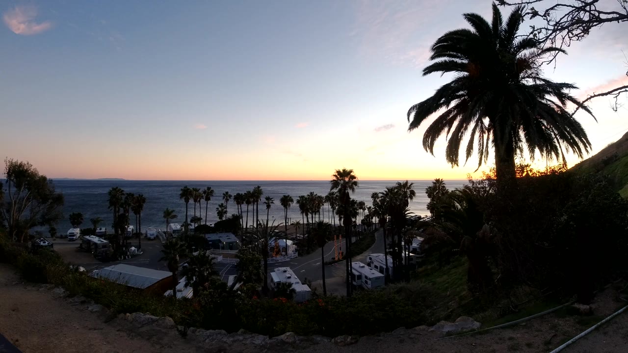 Darker palm silhouette over ocean and beachside structures at sunset.
