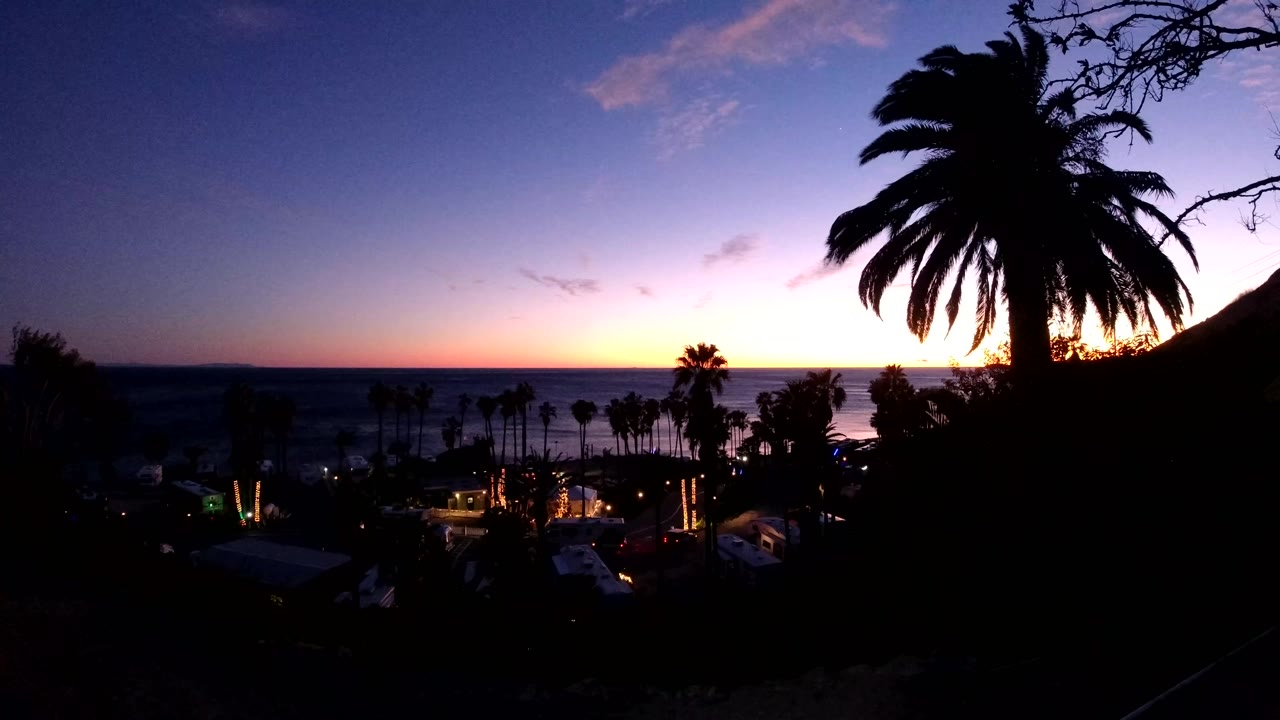 Second frame shows Malibu's ocean horizon under a fading orange band, with the foreground palm still dark against the purple sky and no visible people.