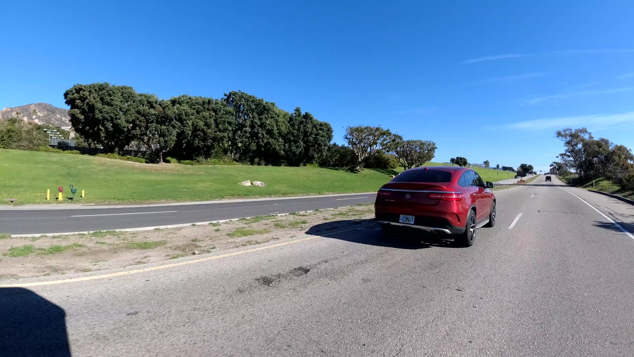 Red vehicle ahead on a road near green hills and trees.