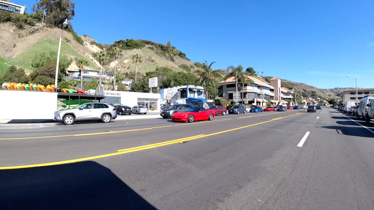 Roadside storefronts and traffic below green and dry hills.