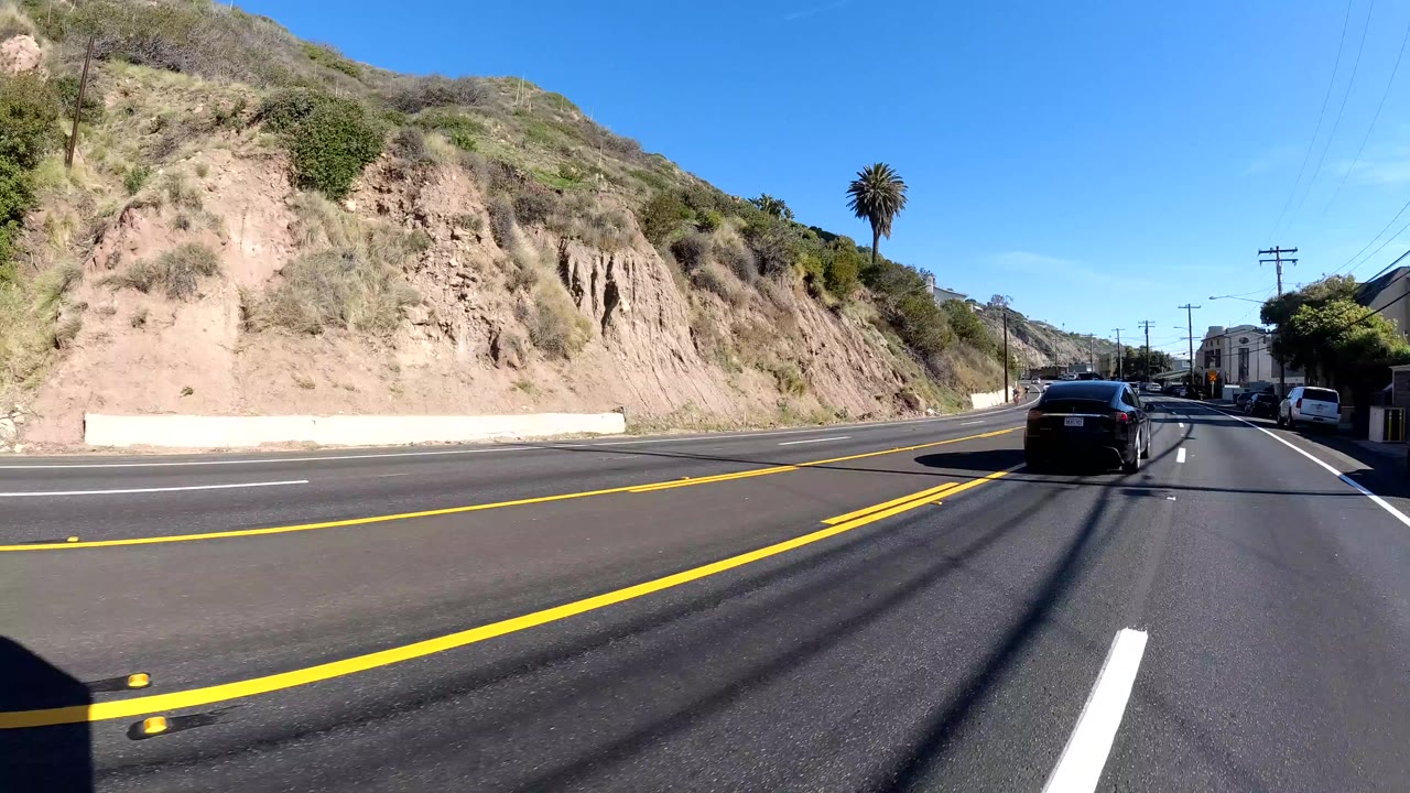 Highway lanes curve past a hillside with cars in the distance.