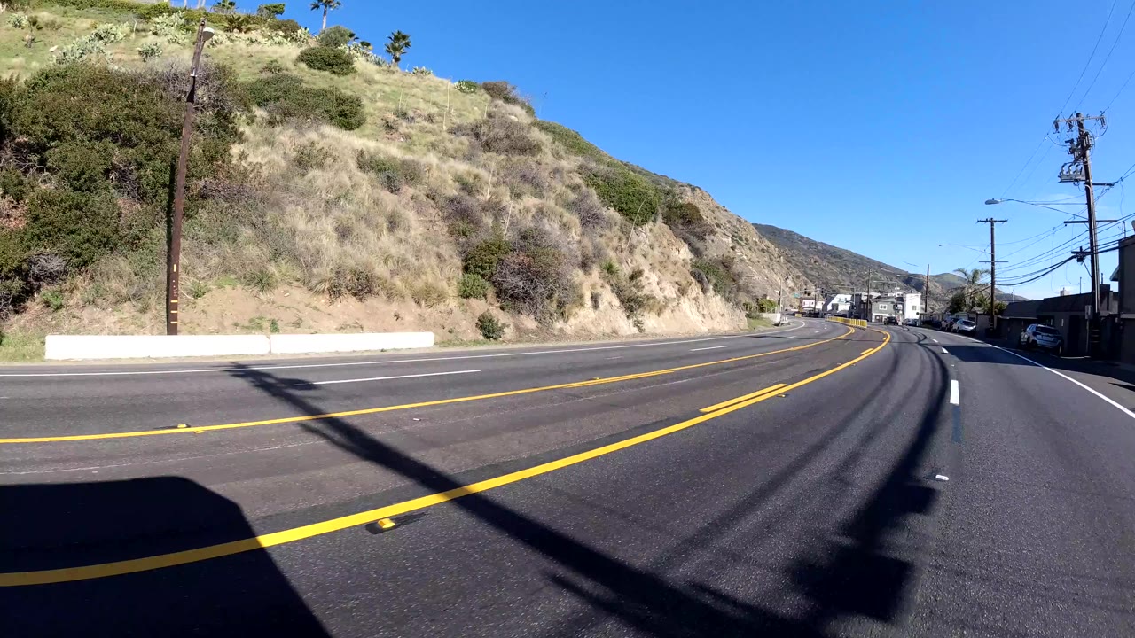 Curving road with hillside, utility pole, and distant traffic.