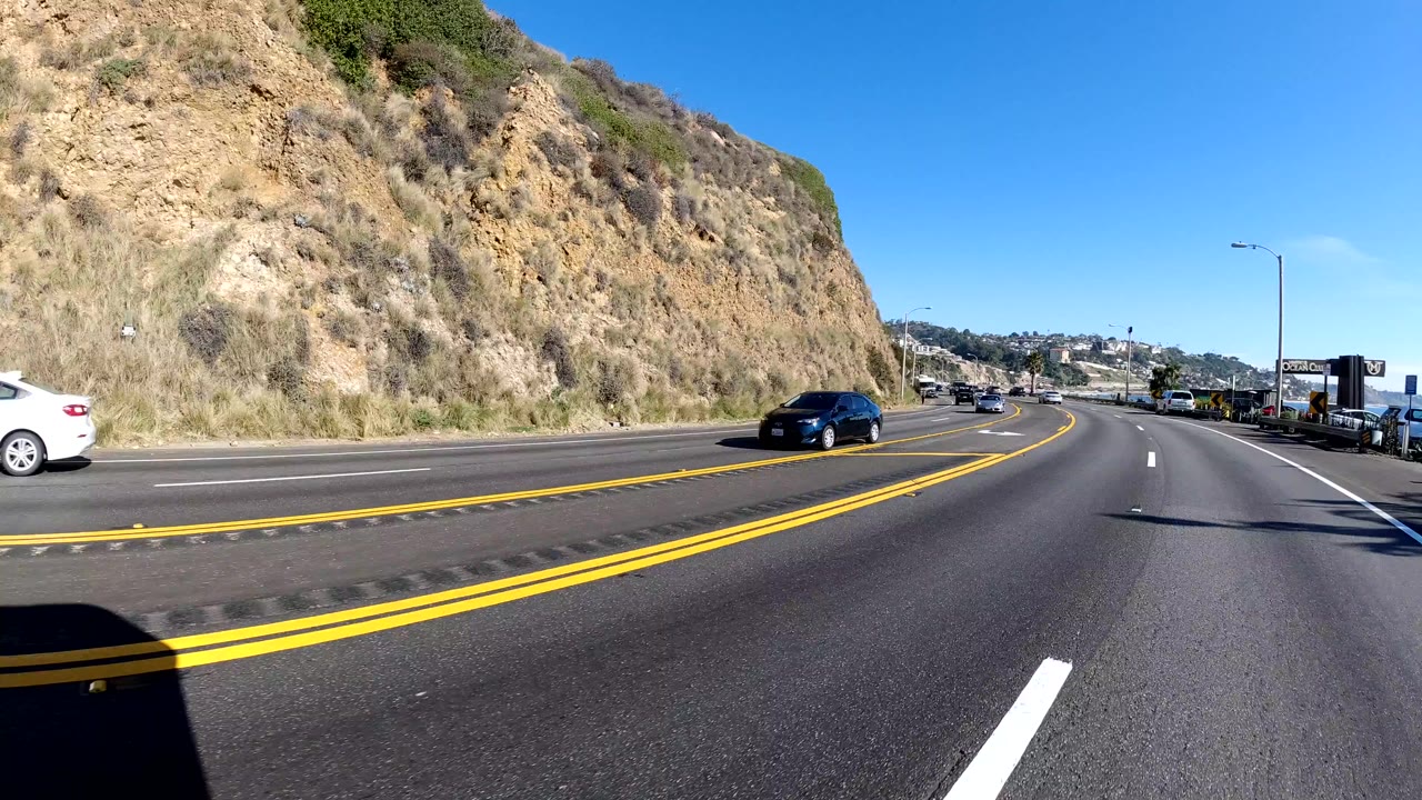 Road curve with double yellow lines, hillside, and several cars ahead.