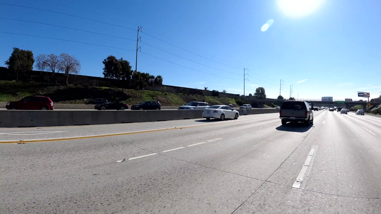 Sunlit freeway with cars, trees, and utility poles along the side.