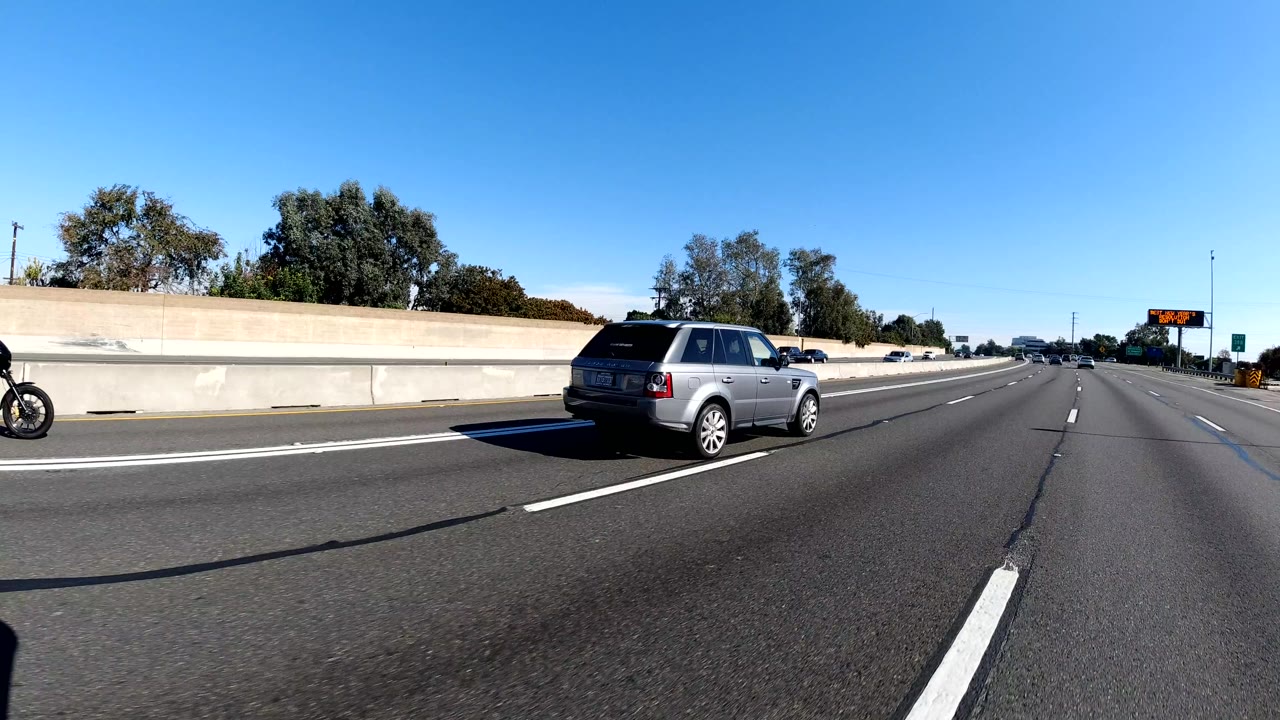 Wide freeway view with gray SUV, motorcycle, concrete barrier, and distant traffic.