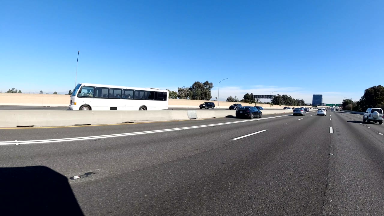 Malibu freeway scene with a white bus on the far side of a concrete divider, scattered cars, overhead signs, and no visible people.