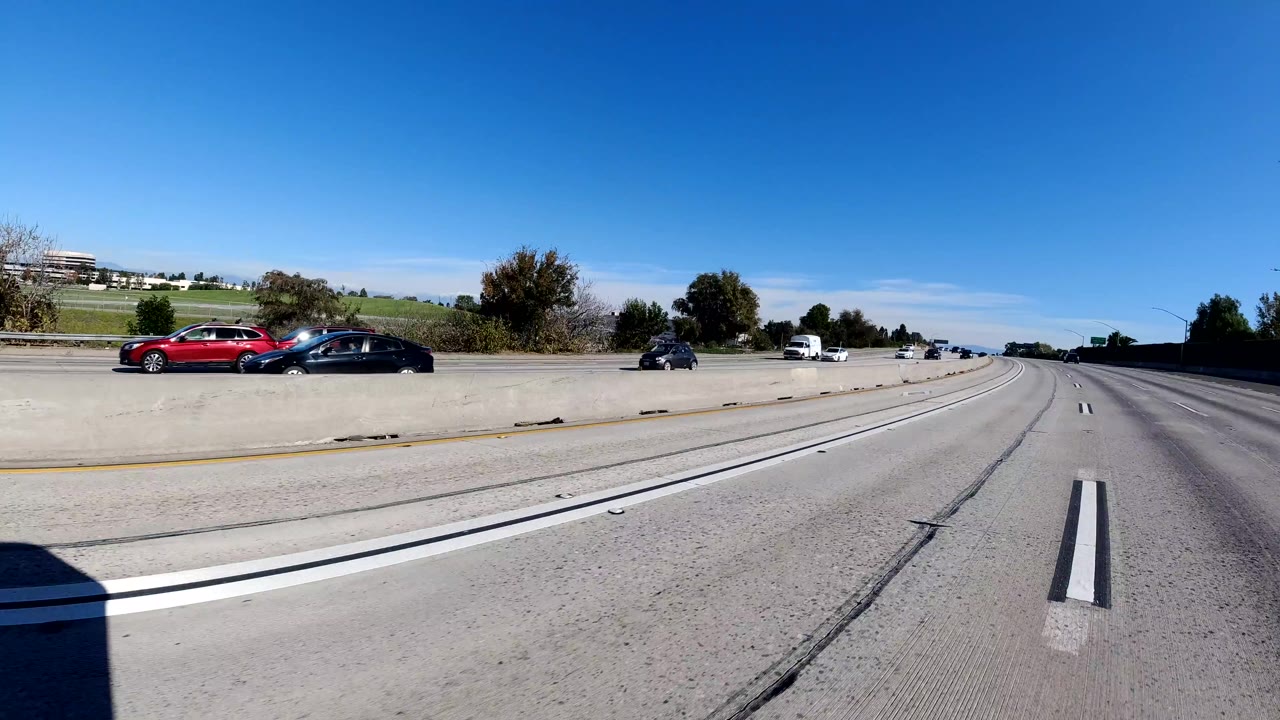 Malibu, California freeway view with a red car, dark sedan, motorcycle, grassy roadside slope, concrete divider, curving lanes, and no visible people.