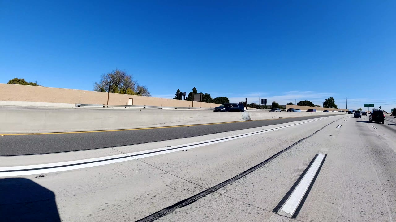 Straight freeway lanes beside a tan sound wall with several vehicles ahead.