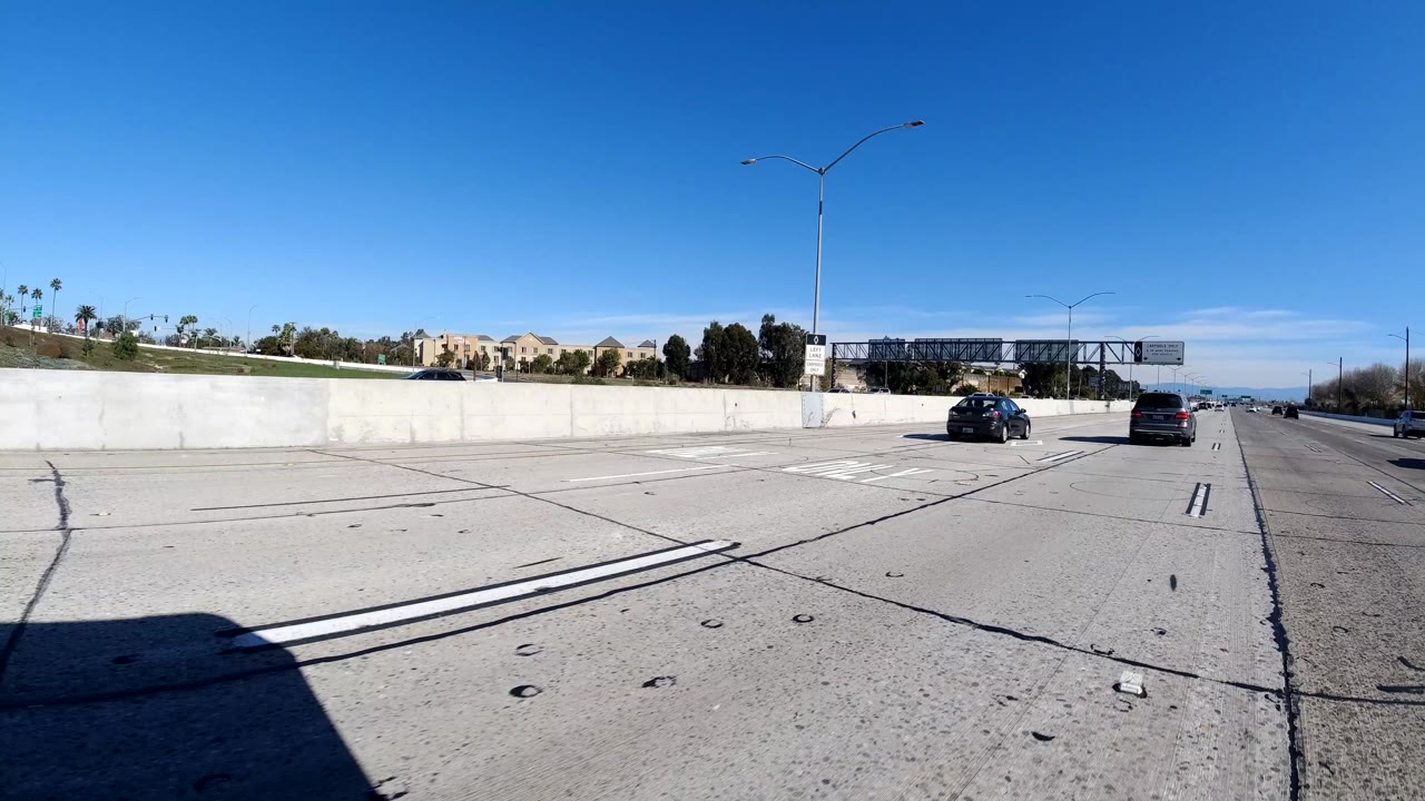Open freeway lanes with overhead signs and cars ahead near a concrete divider.