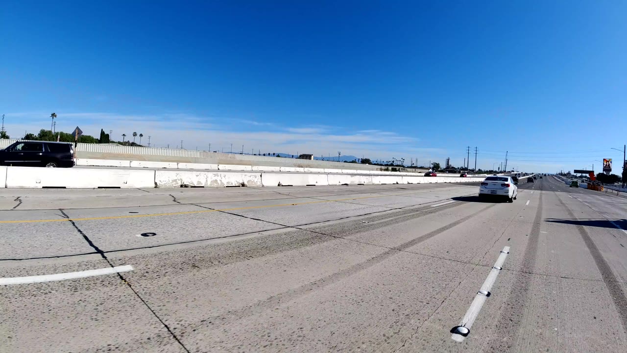 A black SUV travels along the opposite side of a divided Malibu freeway, with broad concrete lanes, a center barrier, overhead sign structures, and no visible people.