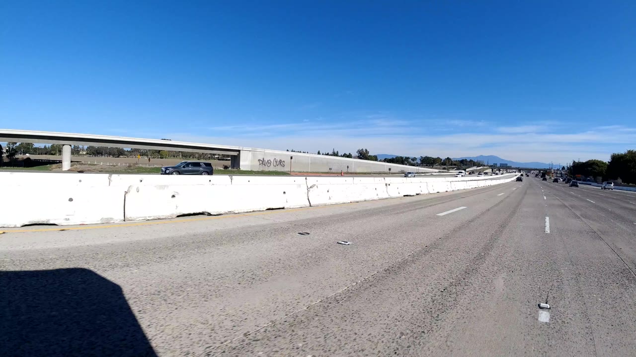 Freeway lane view beside a concrete barrier with an overpass and a dark car.