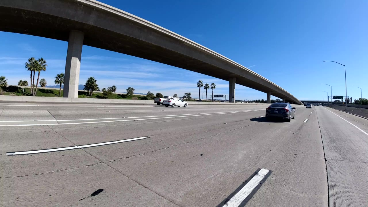 Freeway lanes continue under an overpass with cars in the distance.