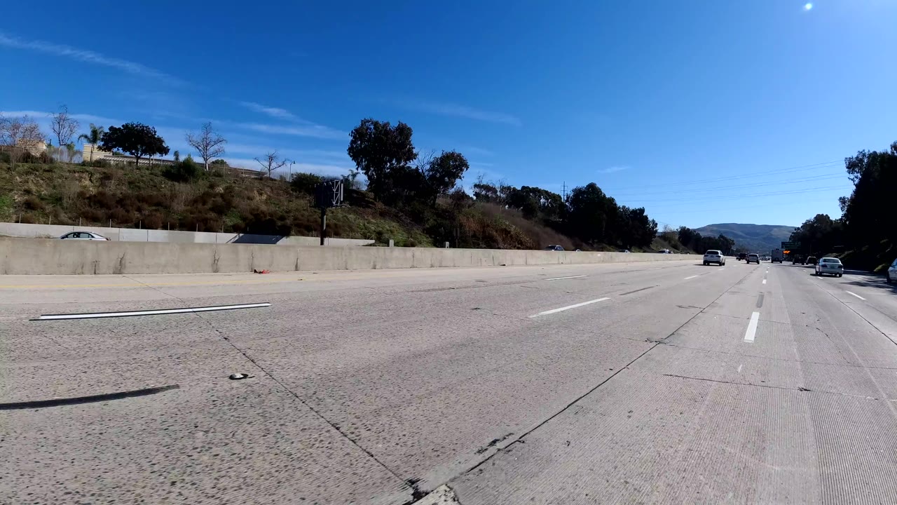 Open highway lanes with roadside slope, trees, and distant traffic