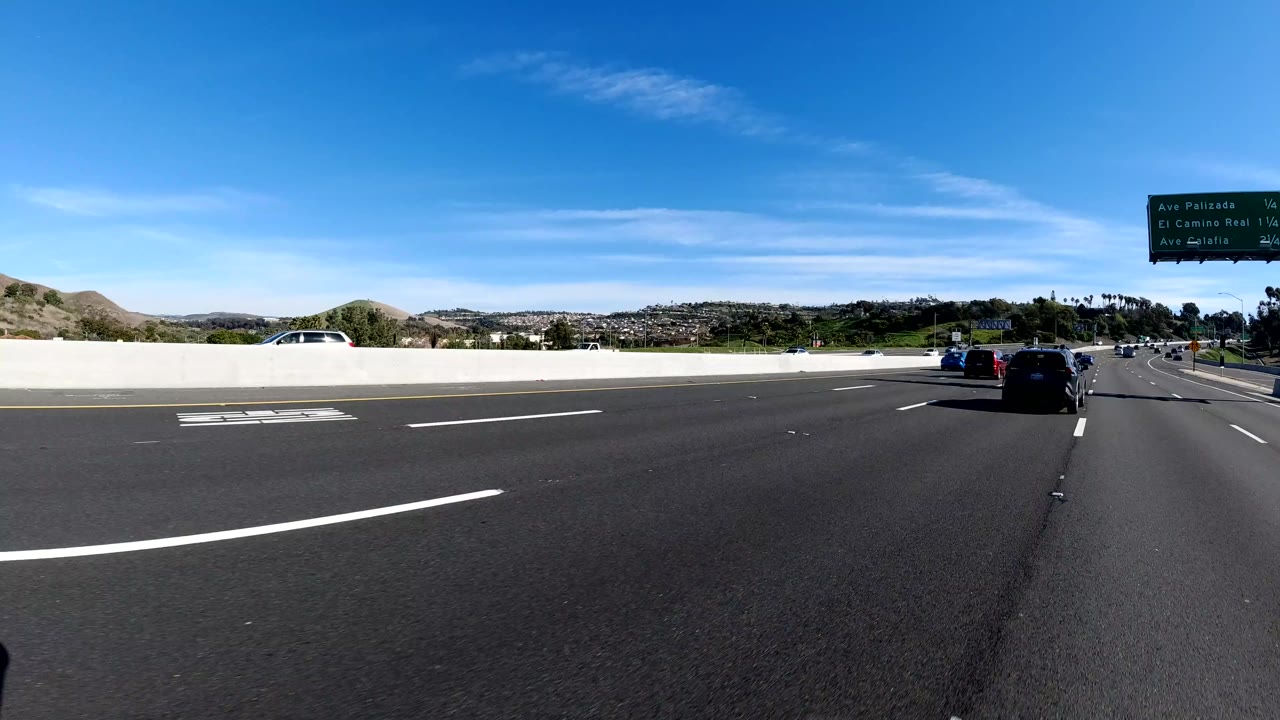 Freeway with cars ahead, low hills, and a green overhead road sign.