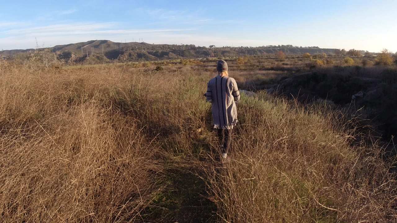 Woman centered on a grassy trail with hills in the distance.