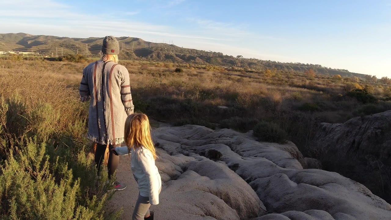 Woman and child remain near brush while facing the open hills.