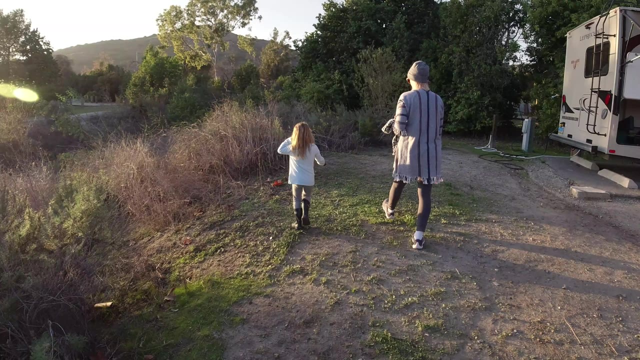 Mother and daughter continue along a dirt path beside brush.