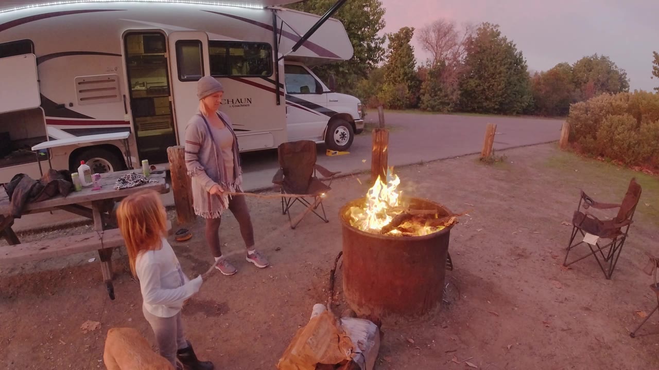 Woman holding a roasting stick as a child faces the campfire.