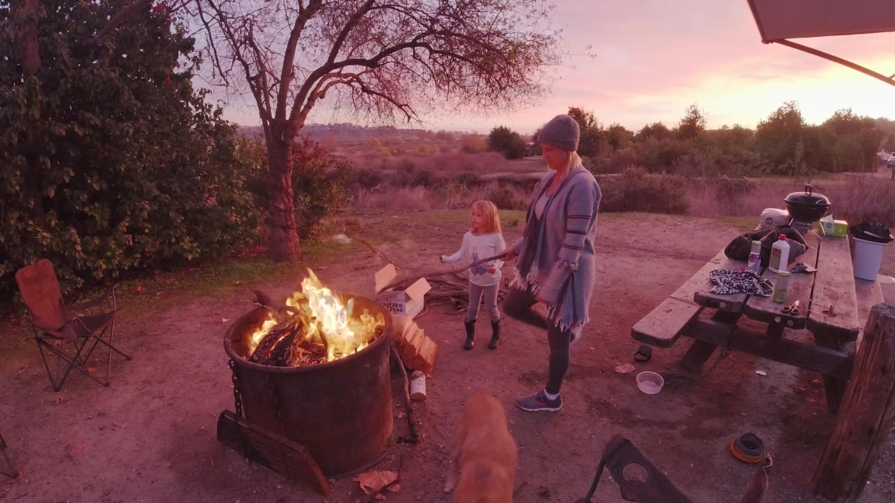 Child stands close to a campfire while a woman watches.