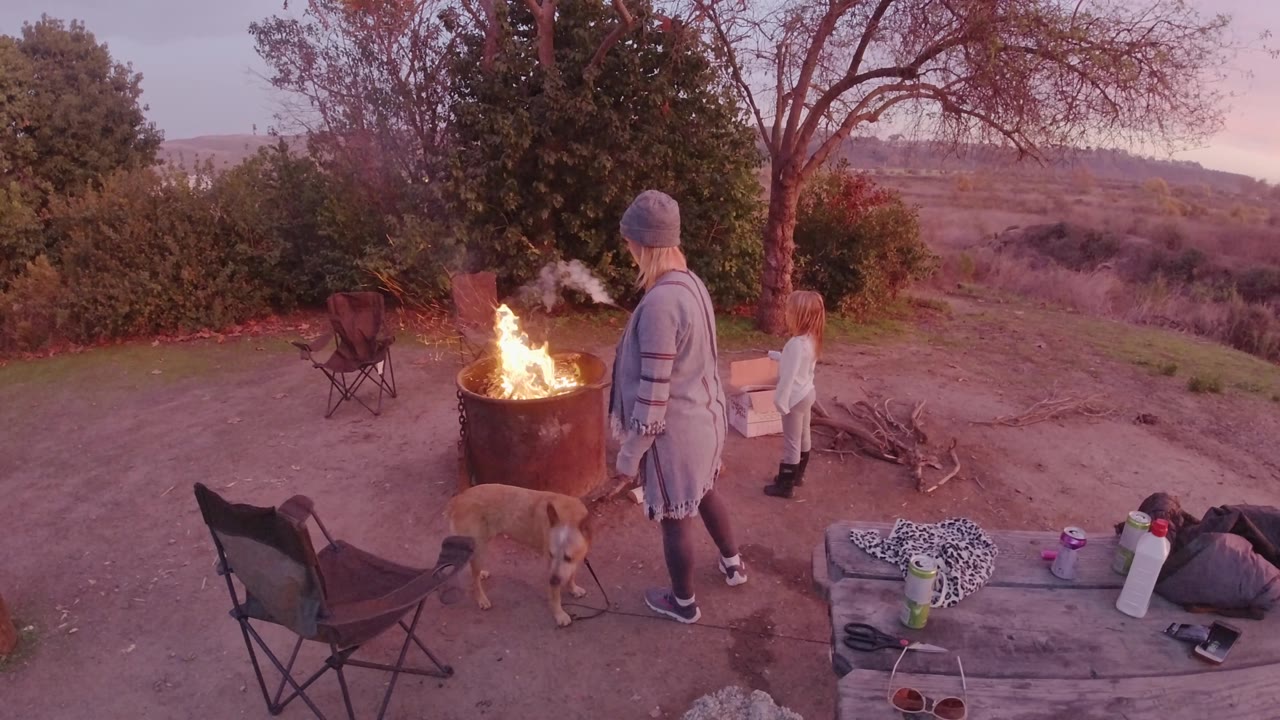 In San Clemente, California, smoke drifts above the flaming barrel while the adult and child watch from the right and the dog remains near the fire area.