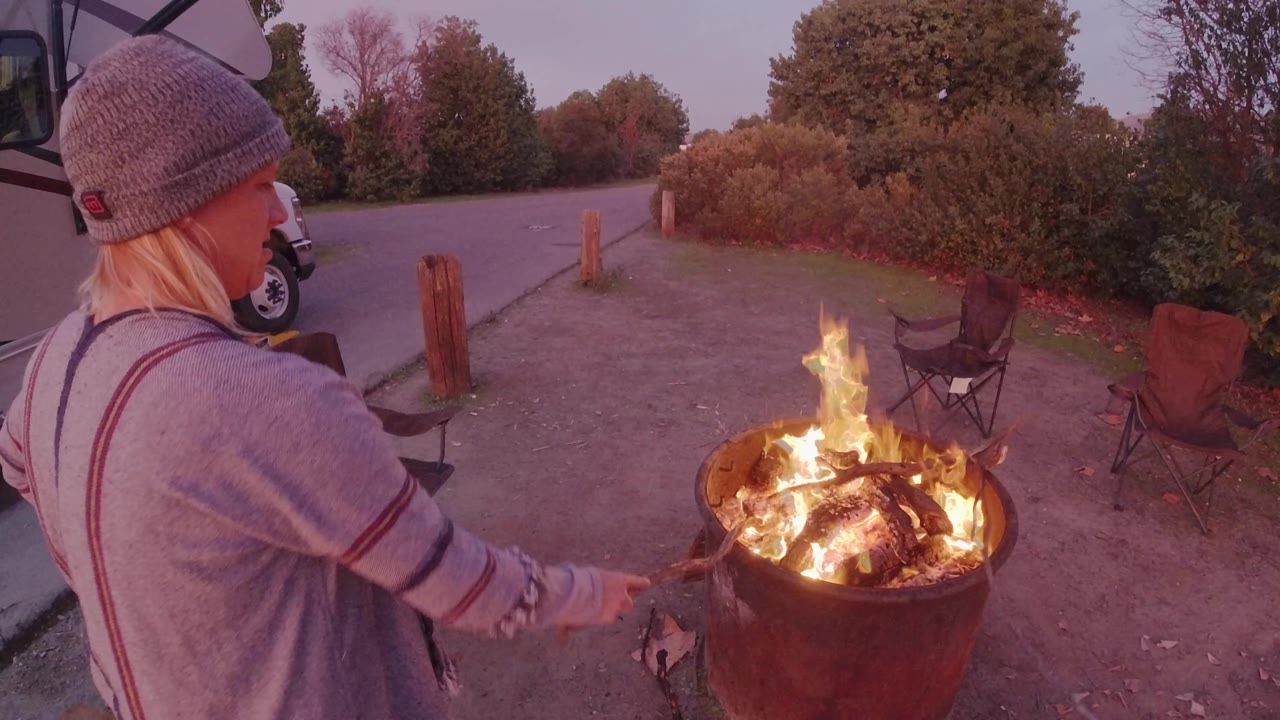 Person reaches toward bright flames in a metal fire pit