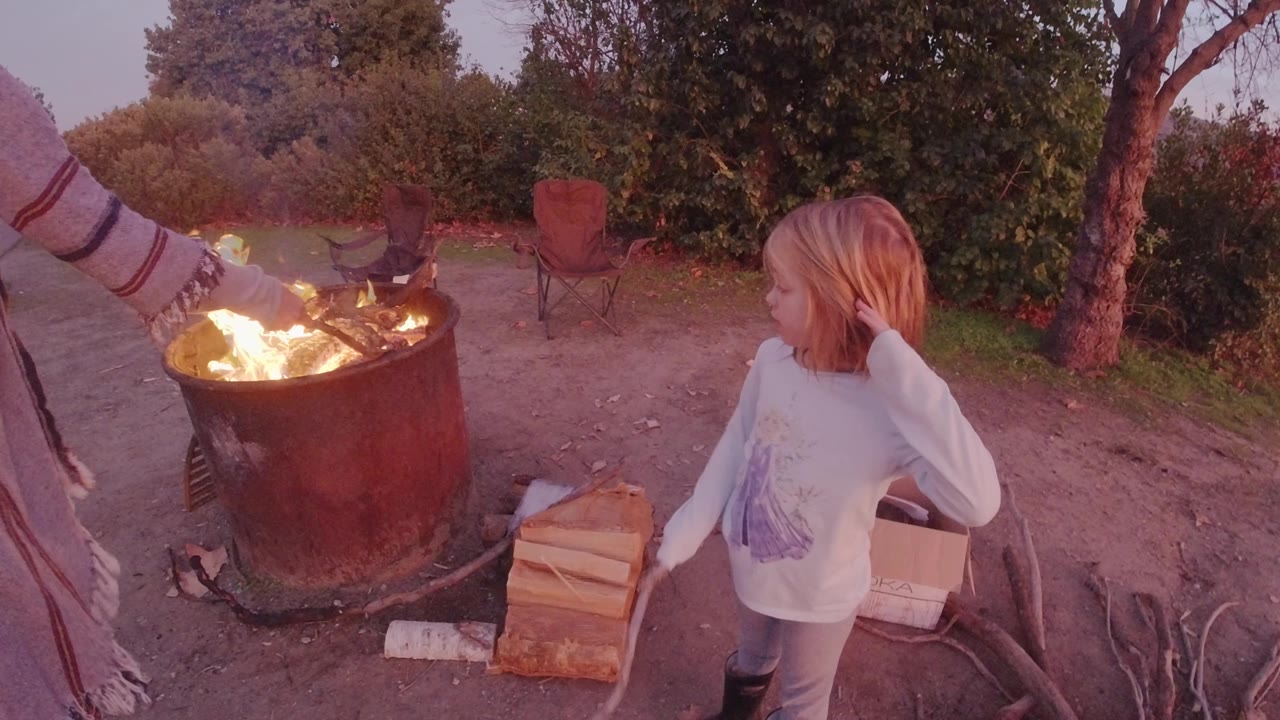 Child turns near a bright campfire with wood stacked on the ground