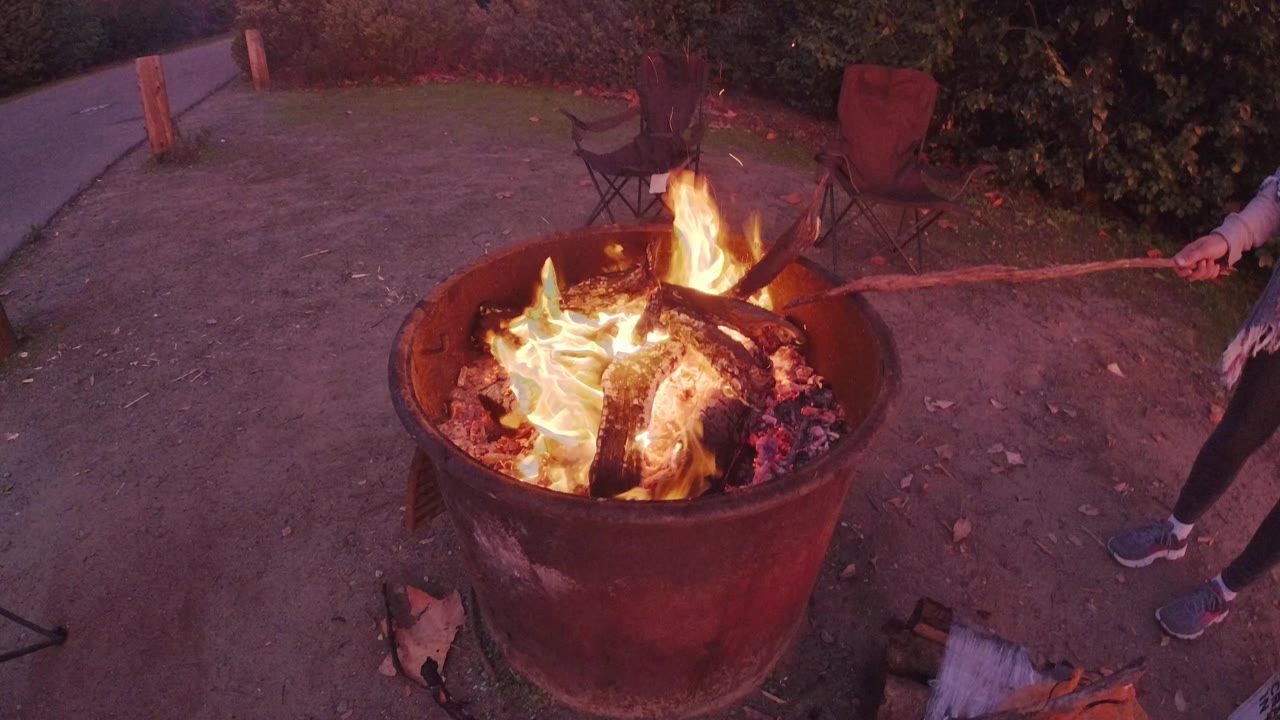 Bright flames rise from logs inside a metal barrel fire pit.