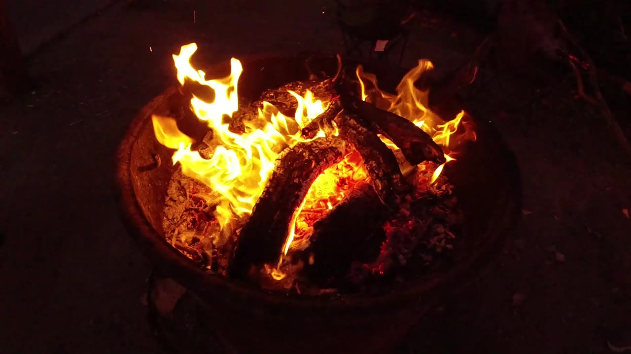 Flames lift above the center log while red embers glow inside the round fire pit in San Clemente, California, with no visible people.