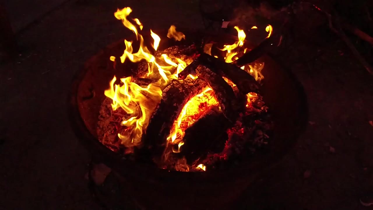 Burning logs with high flames in a dark fire pit.