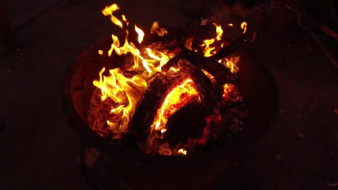 At 0:01, flames curl across the left side of the fire pit while a large red embered log glows near center, with no visible people.