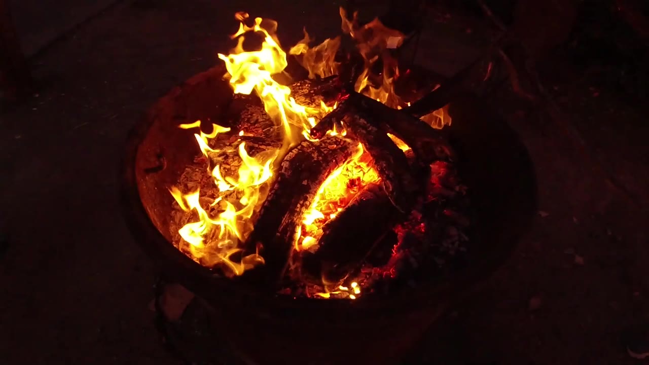 Large flames over glowing wood in a fire pit.
