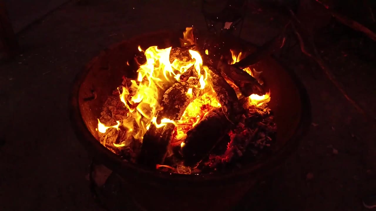 High-angle San Clemente frame of a fire bowl with lower flames spread across the logs, red coals along the lower edge, and no visible people.