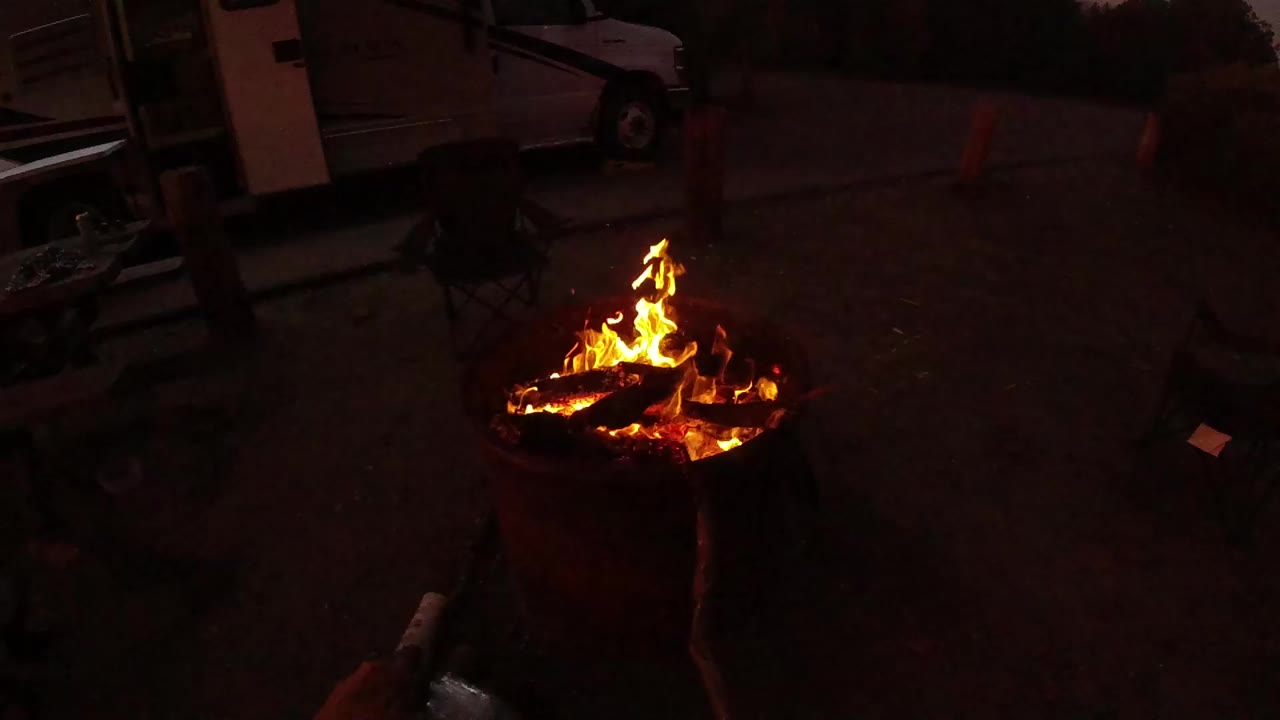 Burning logs in a round outdoor fire pit at low light.