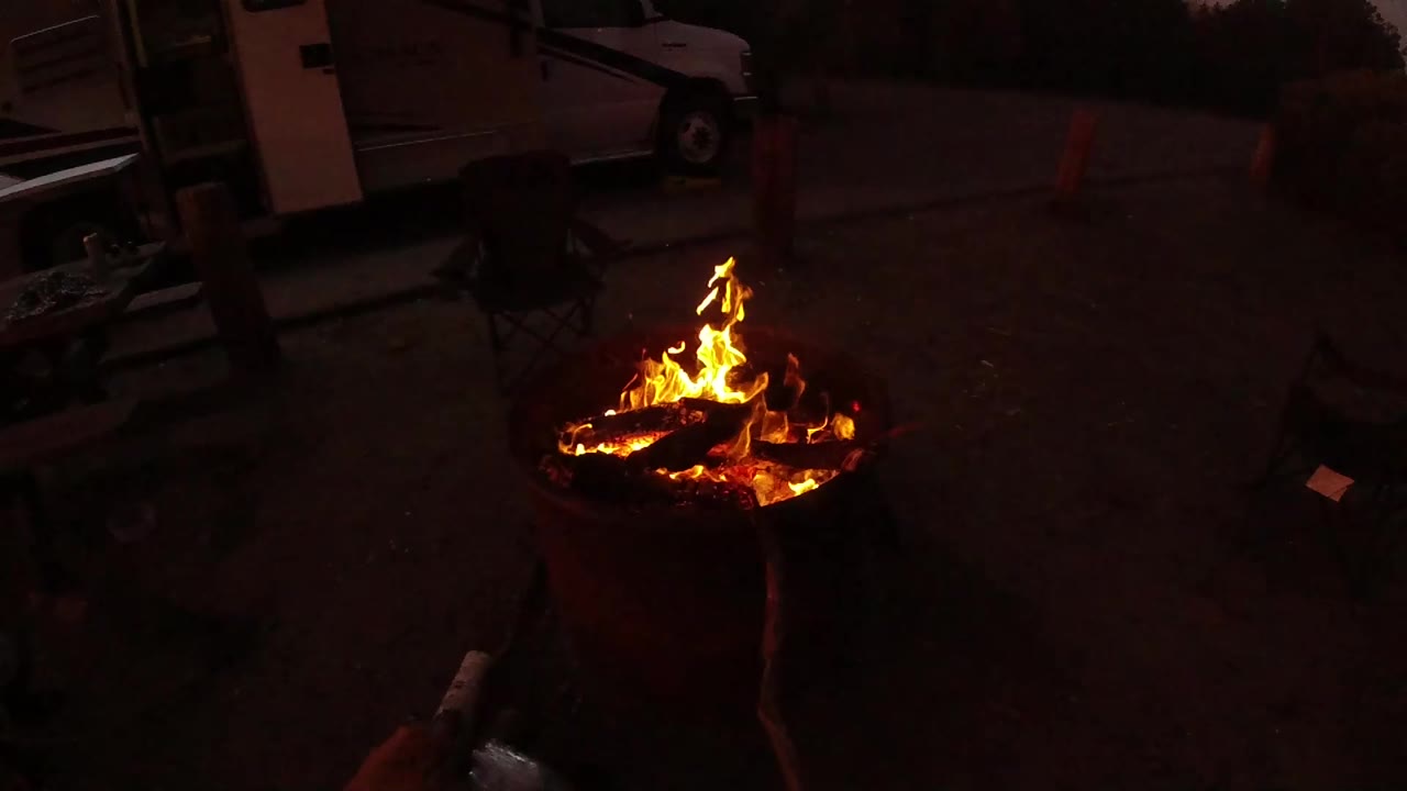 One second in, the fire flares across the charred logs while the surrounding San Clemente campsite or parking area stays mostly dark, with no visible people.