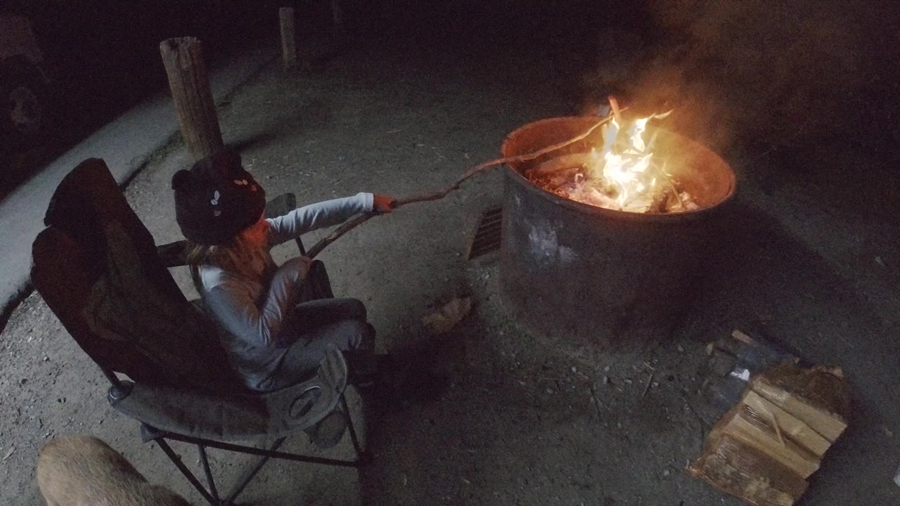 The child remains seated at left in San Clemente, California, with the roasting stick extended into the flames and smoke rising from the metal fire pit.