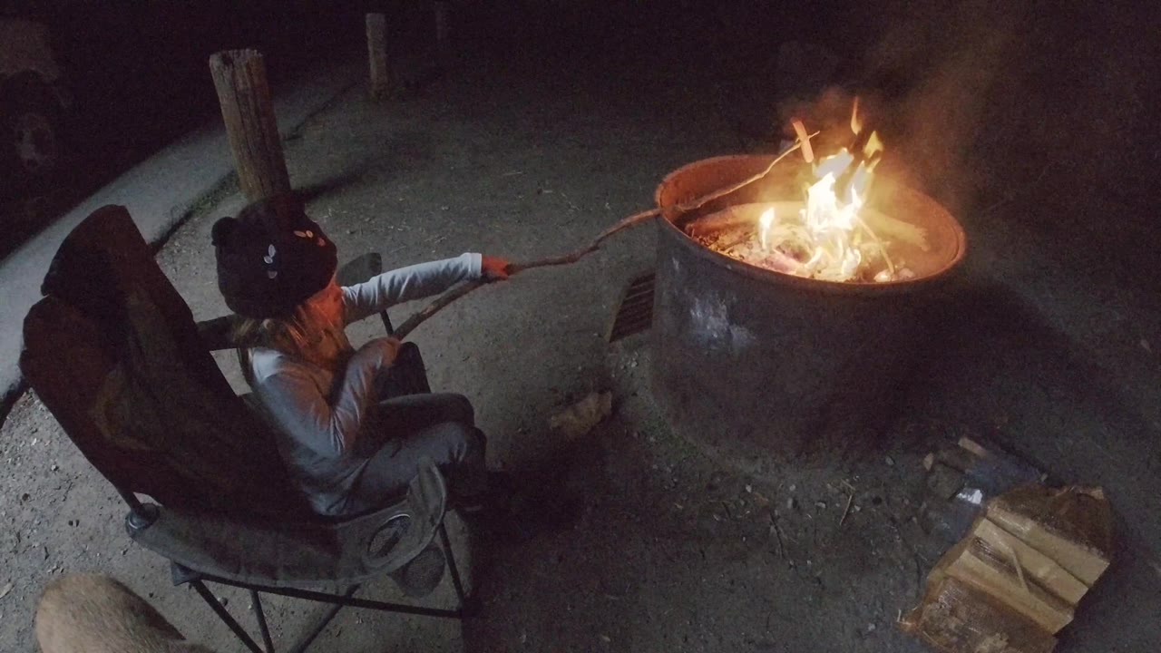 A high overhead frame shows the child at left and the round fire pit at right in San Clemente, California, with brighter flames and smoke above the rim.